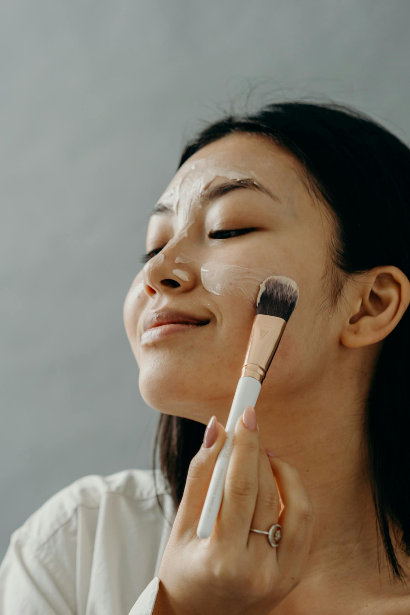 Close-up of a woman applying a face mask using a brush as part of her skincare routine.