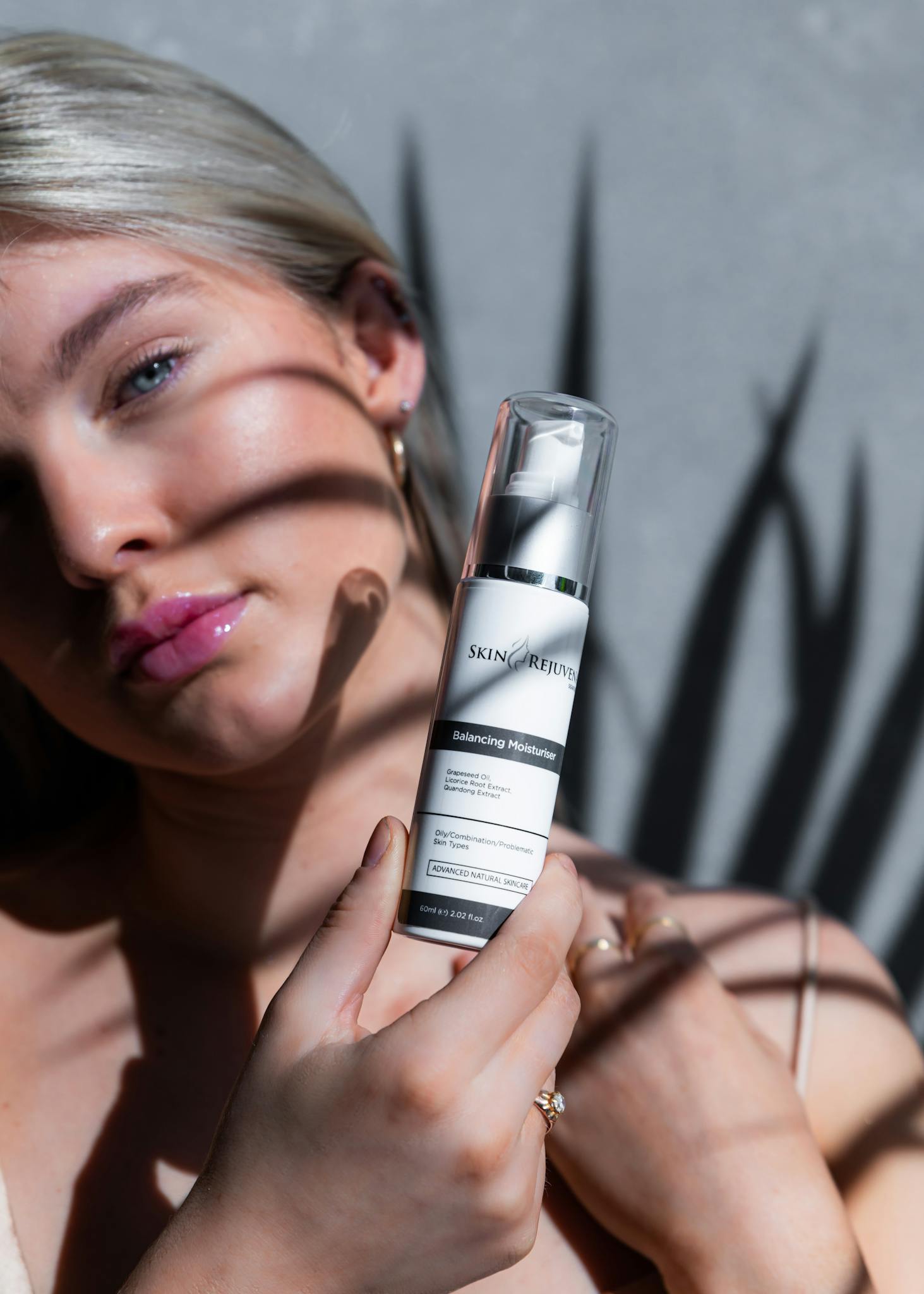 Close-up of a young woman displaying a skincare serum in bright sunlight with artistic shadows.