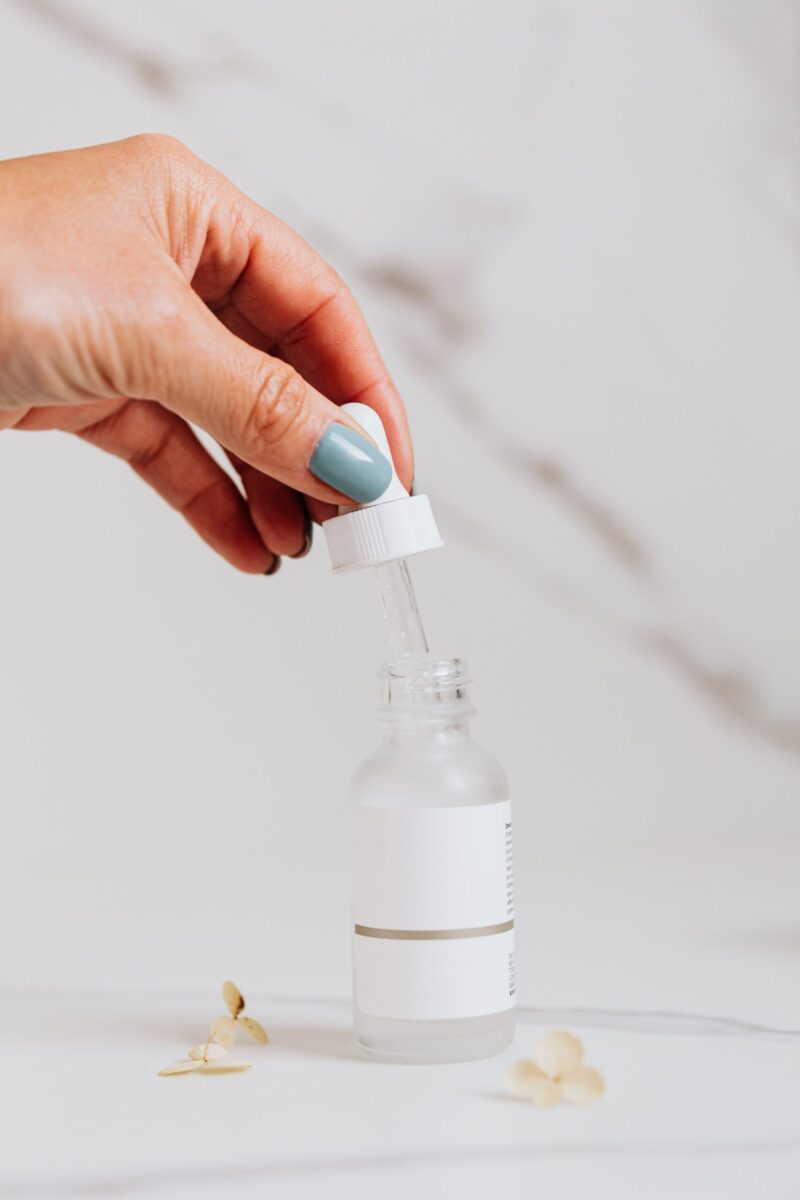 A hand holding a pipette and bottle, applying skincare serum for self-care routine.